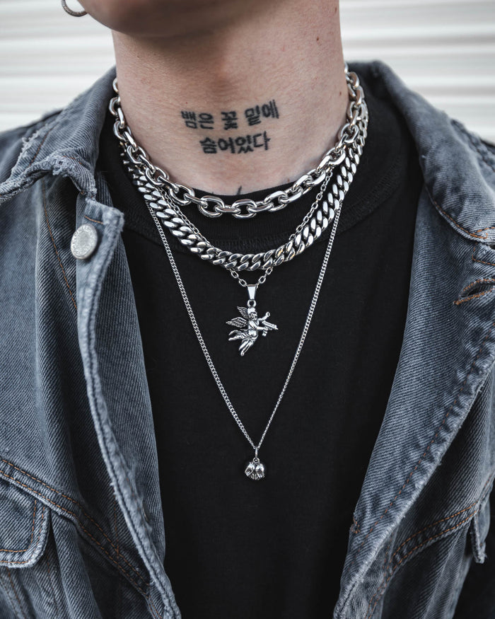Wearing the Dead Love Set by Statement Collective, a person layers the grunge silver-toned necklaces over a black shirt and denim jacket. Above the collar, a tattoo with Korean text is visible on their neck.