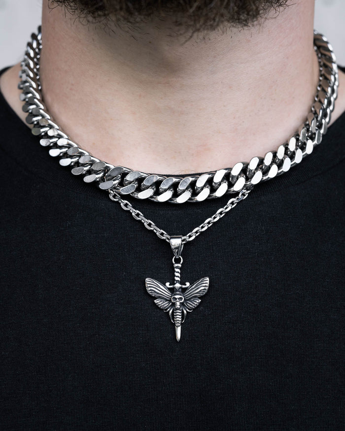 A person wears two silver necklaces—a thick chain and a thinner chain with the Death's Head Moth Pendant—over a black shirt. Only their neck and part of their chin are visible.