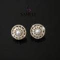 Pair of gold and diamond earrings on a dark background with 'Saheli' branding.