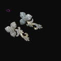 Pair of silver butterfly earrings with clear gemstones on a dark background, featuring the brand 'Saheli'.