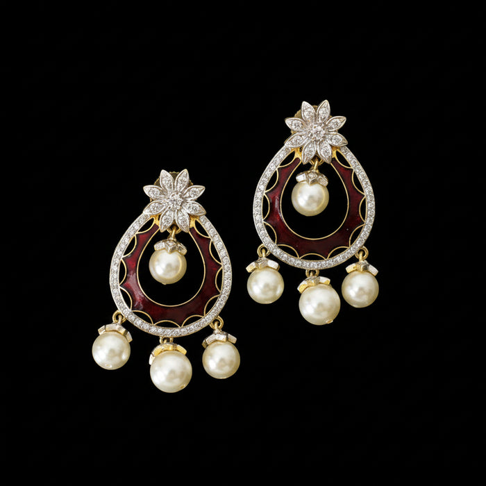A pair of ornate gold and silver-toned statement earrings with deep red enamel inlays, white pearls, and clear rhinestone floral accents, displayed on a dark reflective surface with the Saheli My Best Friend logo in the background.