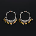 Pair of silver hoop earrings with yellow beads on a brown background