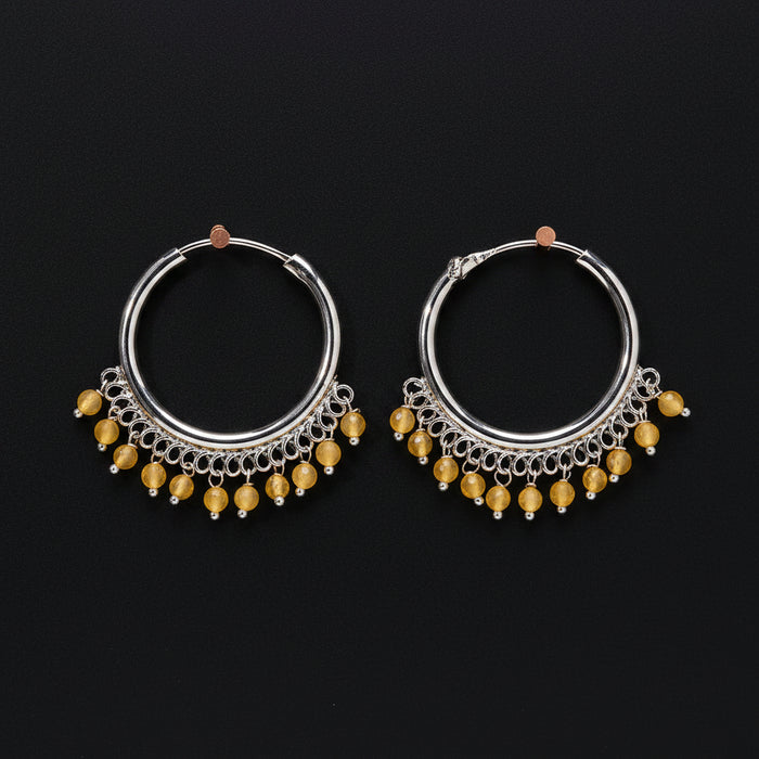 Pair of silver hoop earrings with yellow beads on a brown background
