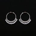 Pair of silver hoop earrings with pearl-like beads on a brown background