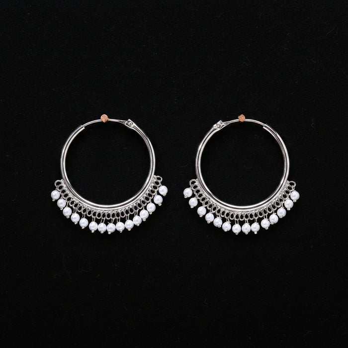 Pair of silver hoop earrings with pearl-like beads on a brown background