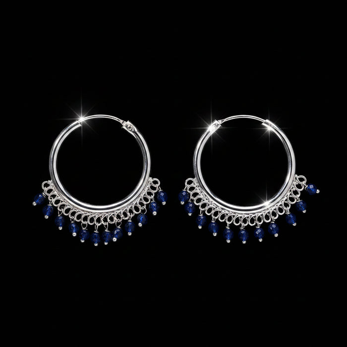 Pair of silver hoop earrings with blue beads on a brown background