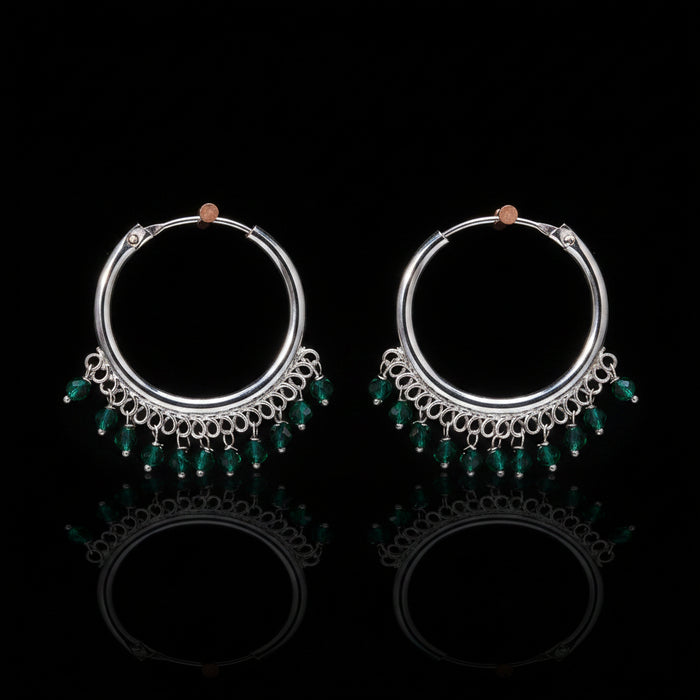 Pair of silver hoop earrings with green beads on a brown background
