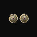 Gold earrings with red gemstones on a black stand, featuring the brand 'SAHELI'.