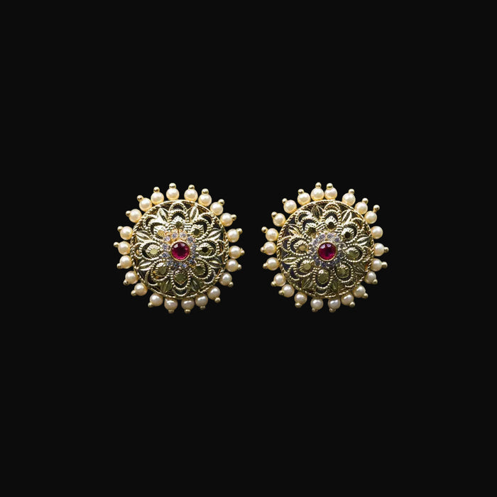 Gold earrings with red gemstones on a black stand, featuring the brand 'SAHELI'.