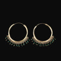Gold hoop earrings with green beads on a dark background, featuring the Saheli brand.