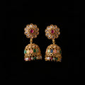 A pair of gold-plated Indian jhumka earrings with floral studs, clear stone accents, and colorful enamel details, displayed on a dark wood background.