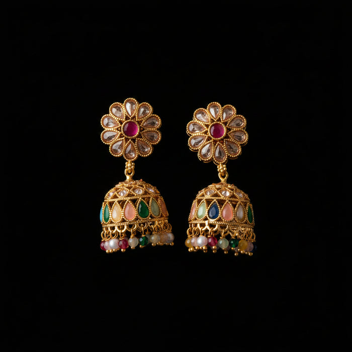 A pair of gold-plated Indian jhumka earrings with floral studs, clear stone accents, and colorful enamel details, displayed on a dark wood background.
