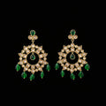 A pair of gold-toned Kundan chandelier earrings with green teardrop beads and clear stones, displayed on a gray Y-shaped stand against a gray background. The brand logo 'SAHELLI MY BEST FRIEND' is visible at the top.