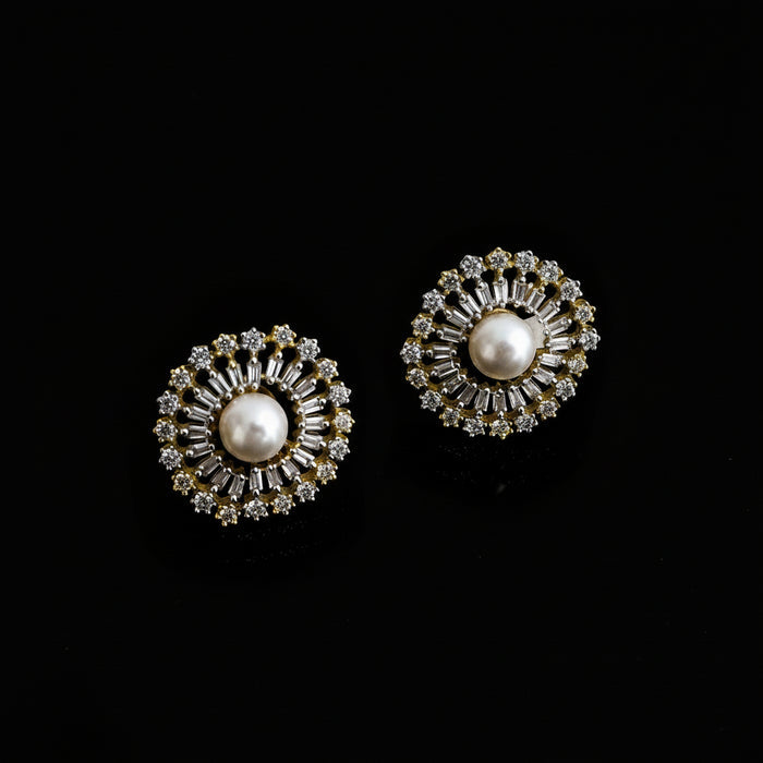 Pair of gold and pearl earrings on a dark background with 'Saheli' branding.