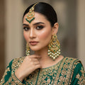 Ornate gold earrings with pearls and green stones on a dark background, featuring the brand 'Saheli'.
