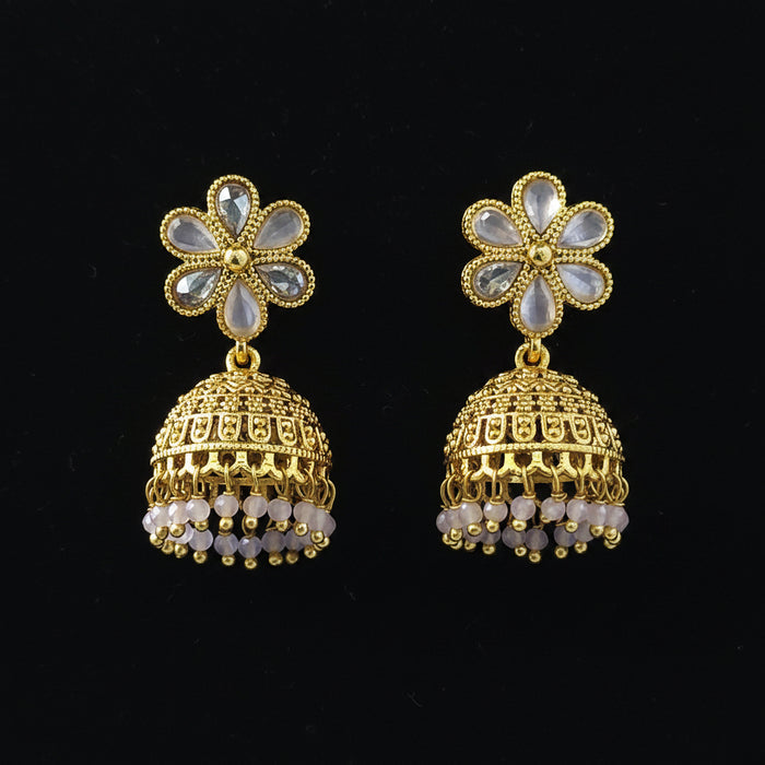 A pair of gold-plated Indian jhumka earrings with light blue stone flower studs and dangling bell-shaped charms, set against a solid blue background.