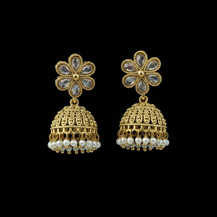 A pair of gold-toned Indian jhumka earrings with clear teardrop stones in the flower-shaped studs and small white pearl-like dangling beads, displayed on a textured blue background.