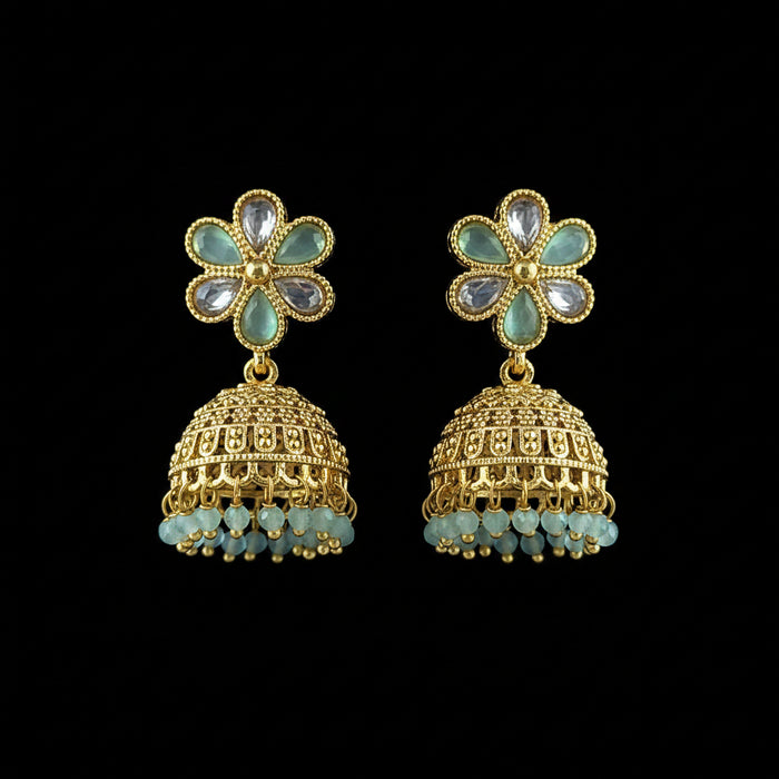 A pair of gold-plated Indian jhumka earrings with light blue stone accents and dangling bead fringes, displayed on a textured blue background.