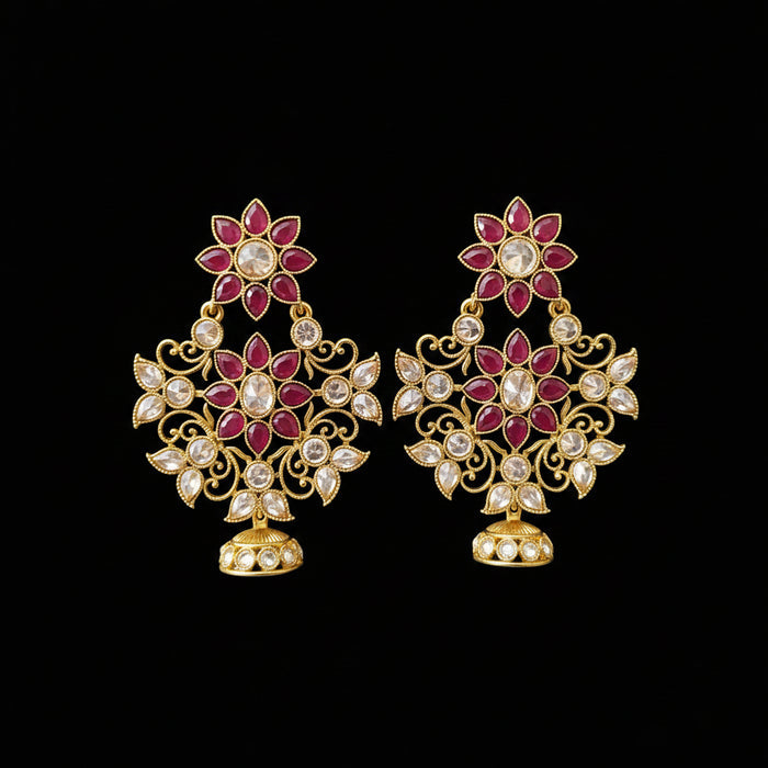 A pair of gold-toned Indian jhumka earrings with red and white stones, displayed on a gray stand with the brand logo 'SAHELL MY BEST FRIEND' above them.