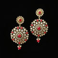 Gold and red earrings on a gray stand with 'Saheli' branding.