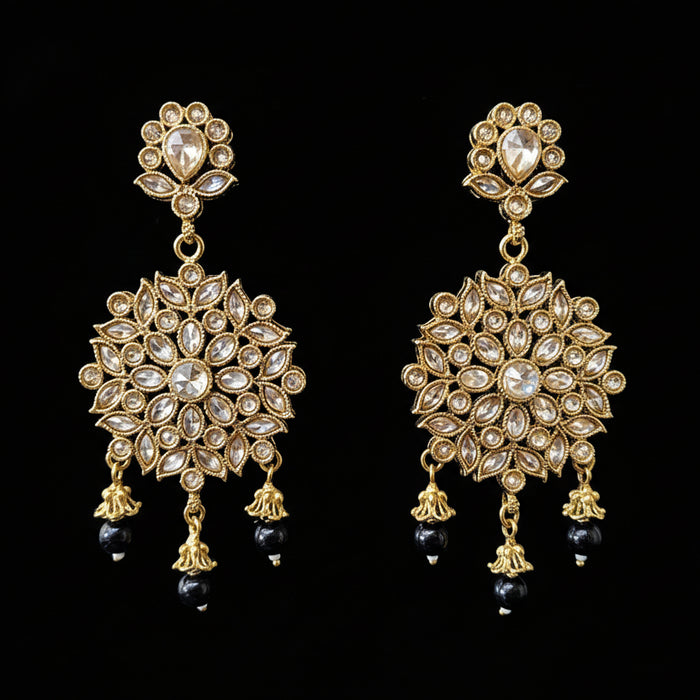 Gold and black earrings on a gray stand with 'SAHELI' branding.