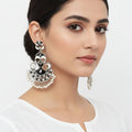 Ornate silver and black earrings with pearl-like beads on a dark background, featuring the brand 'Saheli'.