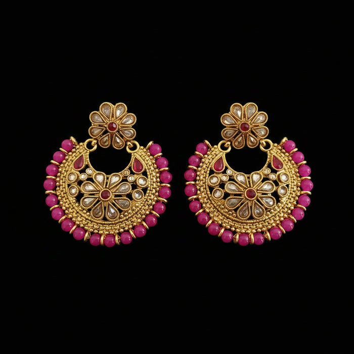A pair of gold-toned Indian jhumka earrings decorated with pink beads and small clear stones, displayed on a dark gray reflective surface with the brand logo 'SAHELI MY BEST FRIEND' at the top.