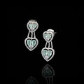 A pair of silver-toned drop earrings with heart-shaped mint green gemstones surrounded by small clear stones, displayed on a gray cushion.