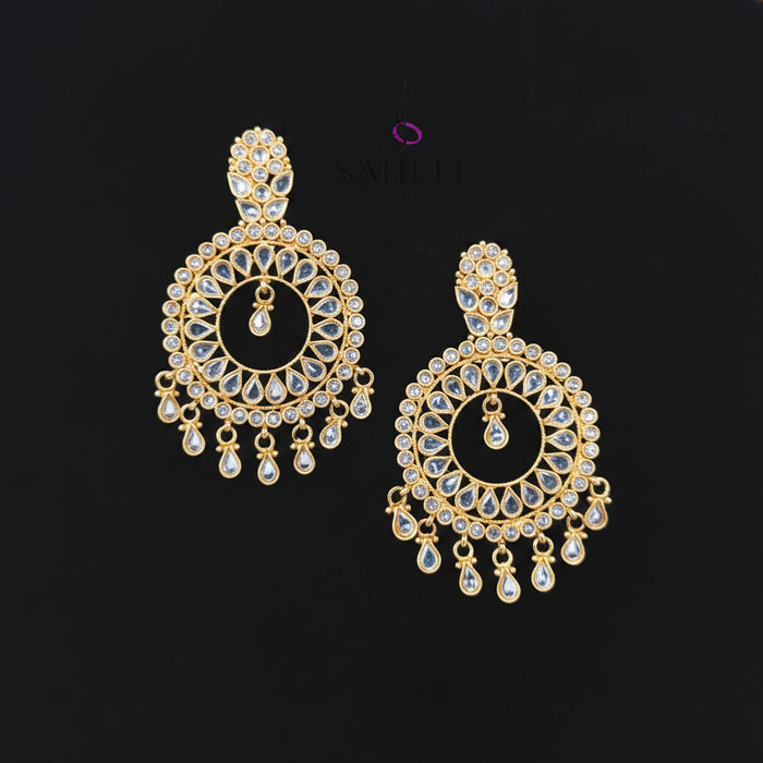 A pair of gold-toned Indian chandelier earrings with clear teardrop crystals, displayed on a black background with the SAHeli Jewellers logo above.
