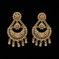 A pair of gold-toned Indian chandbali earrings embellished with clear crystals and light pink stones, displayed on a dark gray reflective surface with the 'SAHELI MY BEST FRIEND' logo at the top.