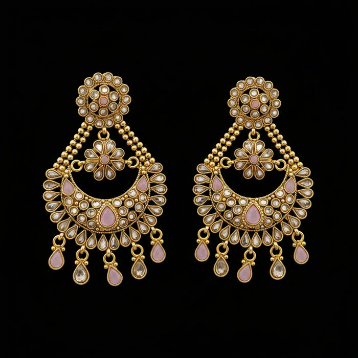 A pair of gold-toned Indian chandbali earrings embellished with clear crystals and light pink stones, displayed on a dark gray reflective surface with the 'SAHELI MY BEST FRIEND' logo at the top.