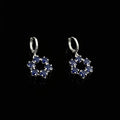 Pair of silver earrings with blue gemstones on a gray background, featuring the brand 'Saheli'.