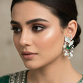 Pair of silver earrings with green and clear gemstones on a gray cushion