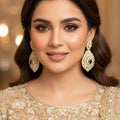 Gold and diamond earrings on a dark background with 'Saheli' branding.