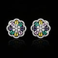 A pair of round floral stud earrings in silver-tone metal, featuring a multicolor gemstone center with yellow, green, purple, and pink stones surrounded by clear crystals, set against a solid blue background.