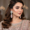 Pair of earrings with diamond-like stones and pink teardrop shapes on a gray cushion.