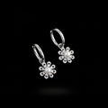 A pair of silver hoop earrings with dangling flower charms, each featuring a central white pearl surrounded by small clear rhinestones, displayed on a white card over a blue background with green leaves in the corner.