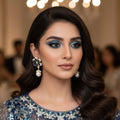 Pair of earrings with blue gemstones and pearl drops on a gray stand, branded 'SAHELI'.