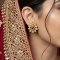 Gold floral earrings with pink gemstones on a dark background, branded 'Saheli'.