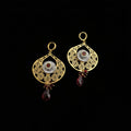 Gold earrings with red gemstones on a dark background, featuring the brand 'Saheli'.