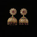 A pair of gold-plated Indian jhumka earrings decorated with clear crystals, pink gemstones, and green gemstones, displayed on a solid dark pink background.