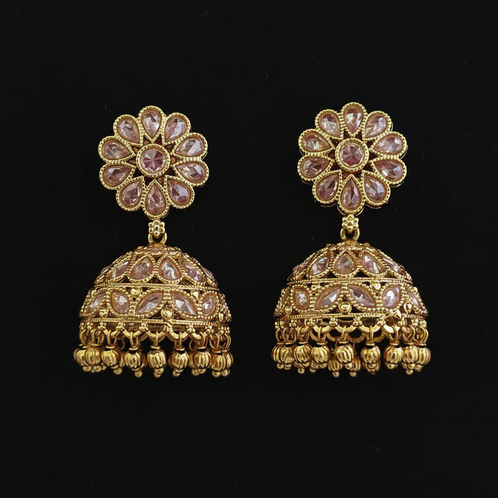 A pair of gold-plated Indian jhumka earrings decorated with clear stones in a floral pattern and a dome-shaped jhumka with hanging bell details, set against a solid dark red background.