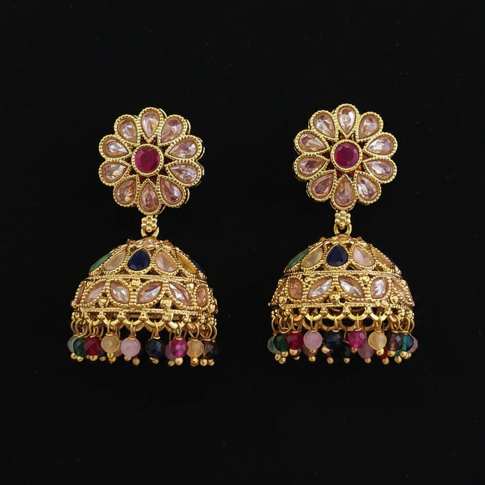A pair of ornate gold-plated Indian jhumka earrings decorated with pink, blue, and multicolor stones, displayed on a solid dark pink background.