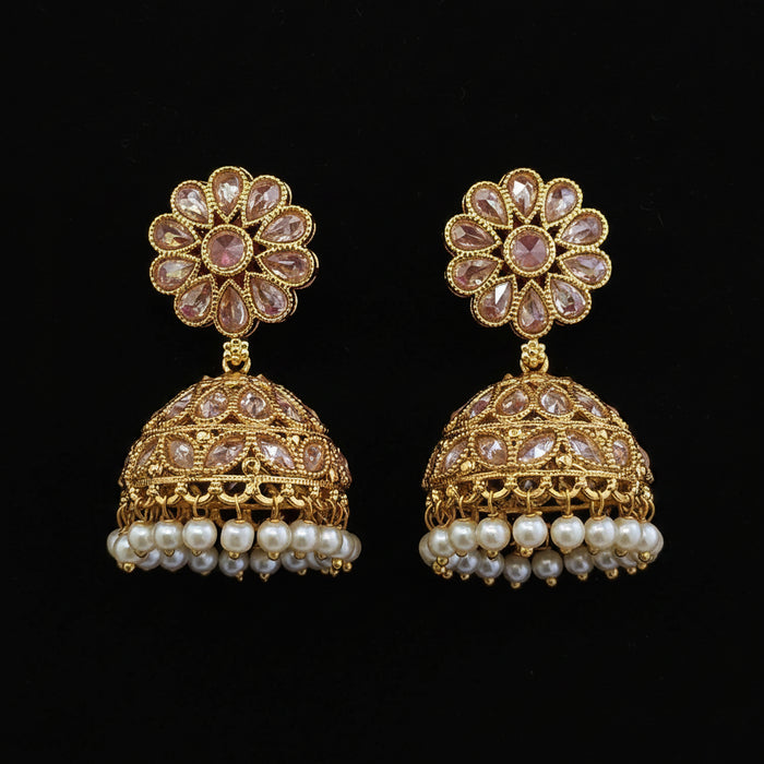 A pair of ornate gold jhumka earrings with pink gemstone floral studs and dangling pearl rows, displayed on a solid dark red background.