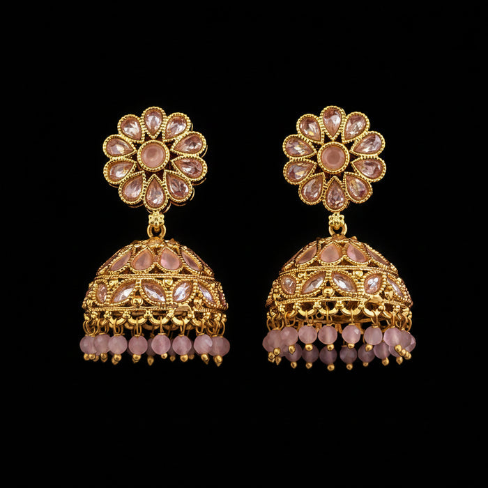 A pair of ornate gold-toned jhumka earrings with pink stone accents and dangling bead chains, displayed on a solid red background.