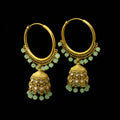 Gold hoop earrings with green gemstones on a black stand