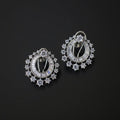 A pair of silver-toned oval hoop earrings adorned with clear baguette and round-cut stones, displayed on a dark reflective surface.