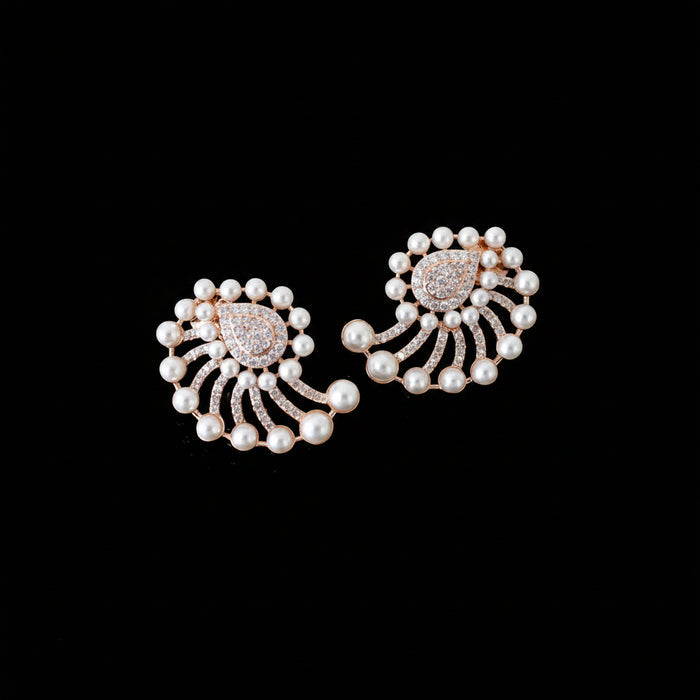 A pair of ornate pearl and rose gold earrings with a floral or fan-like design, displayed on a dark reflective surface.