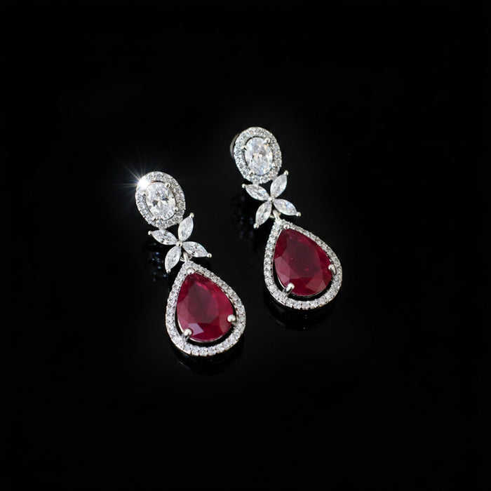 Pair of teardrop-shaped earrings with red gemstones and silver accents on a dark background