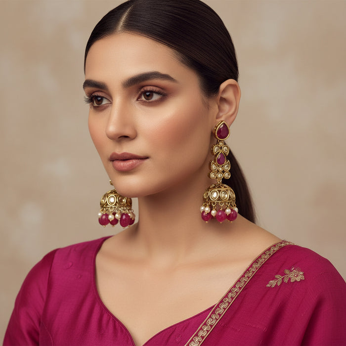 Ornate gold and red earrings on a black stand with 'SAHELI' branding.